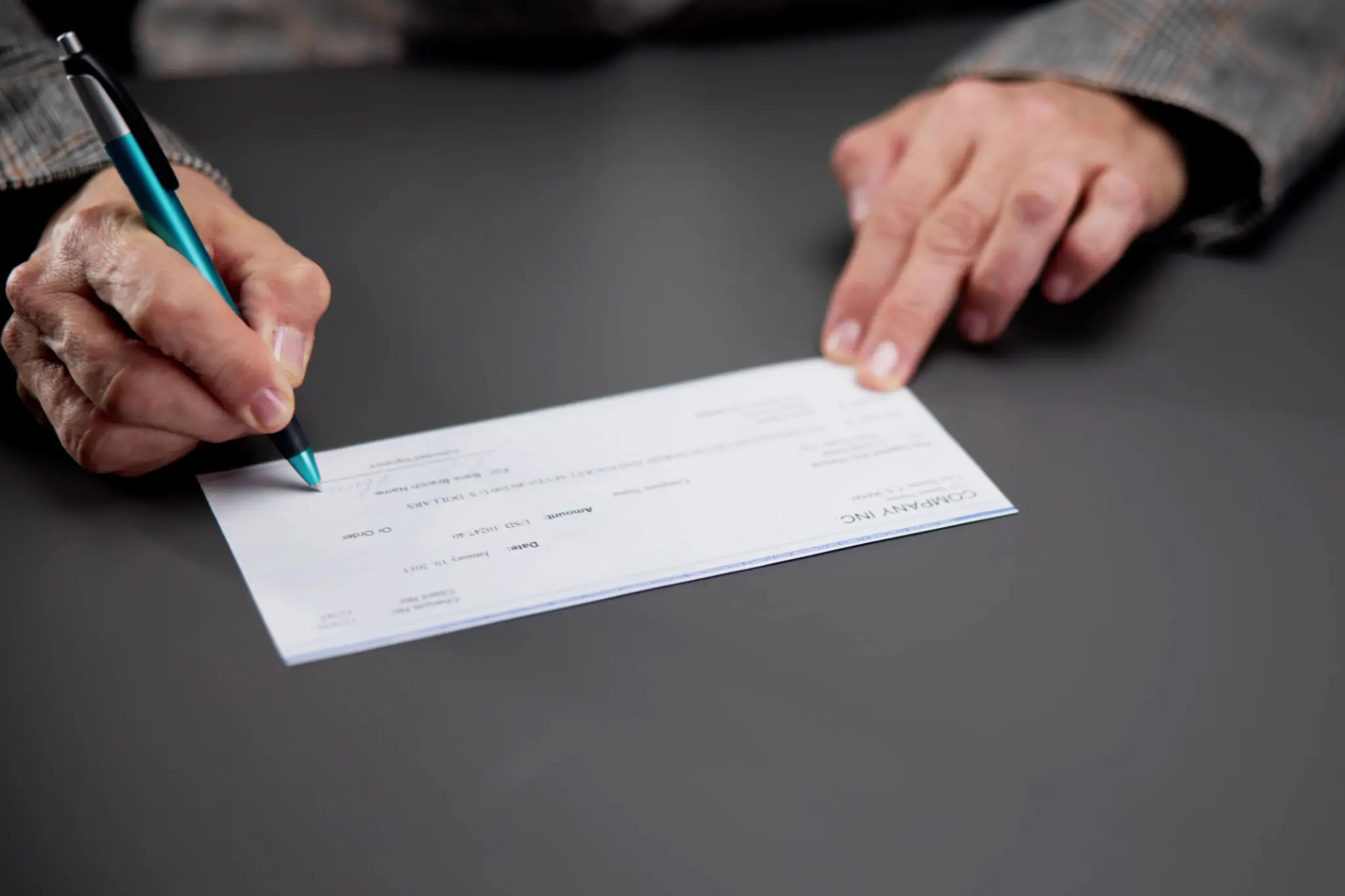 Person writing on a check with a pen on a dark surface.